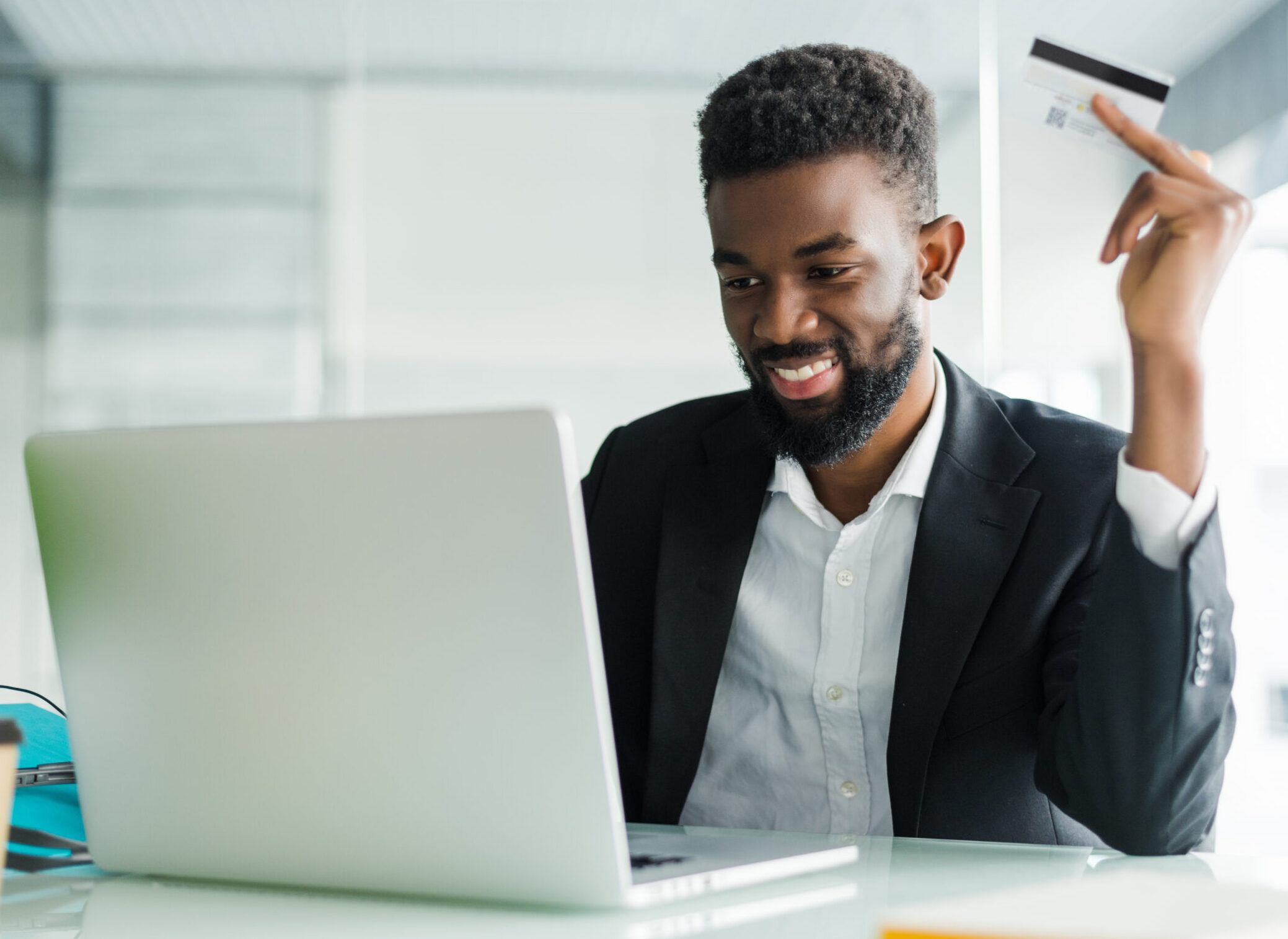 Successful African businessman sitting at a laptop and holding credit card in hand until businessman doing orders through the Internet